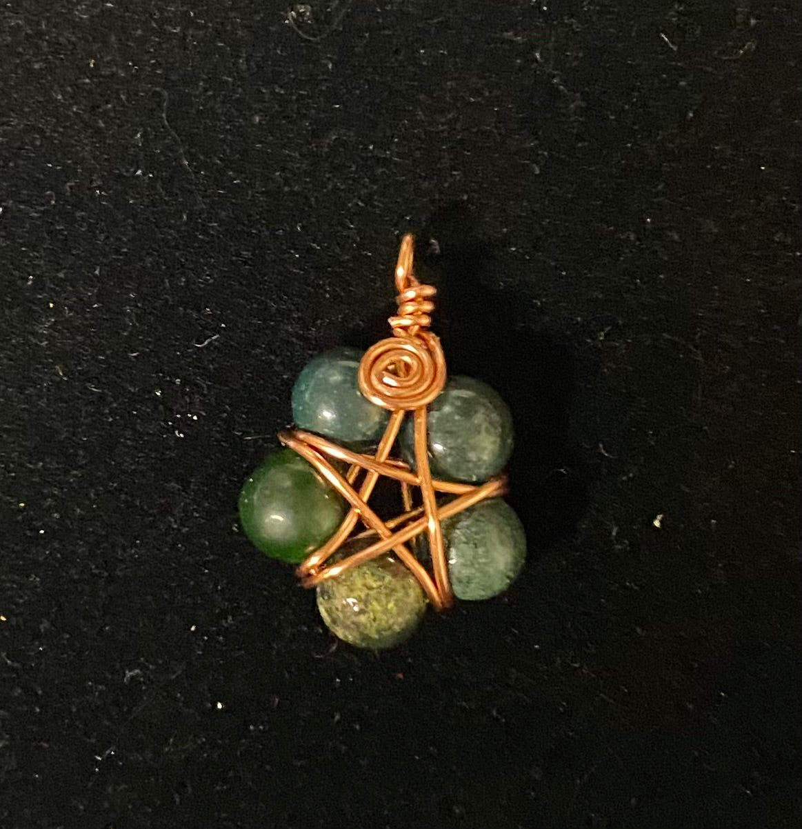 Pendant with green beads and copper wire wrapping on a black background