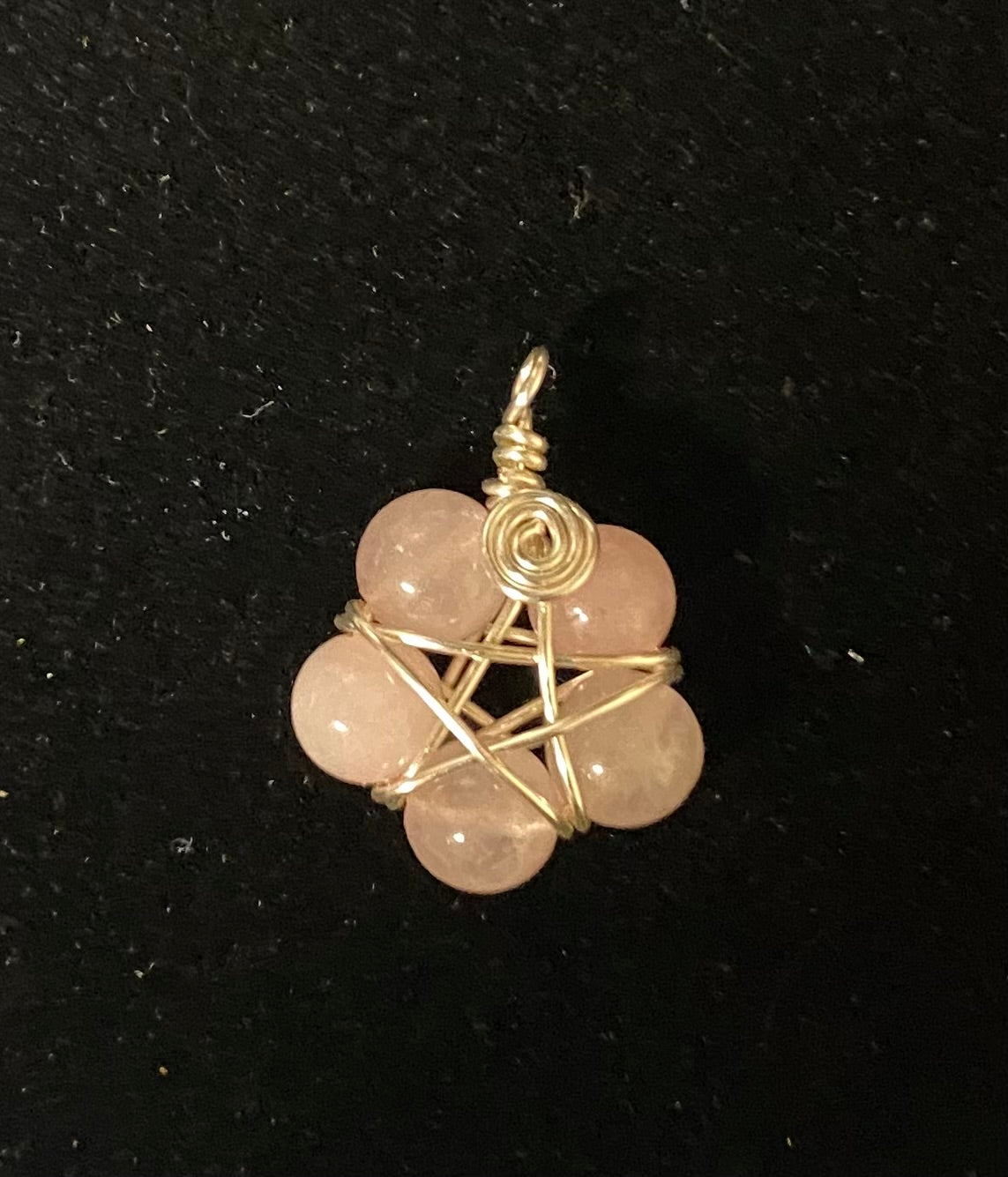 Rose quartz crystal pendant with silver wire wrapping on a black background