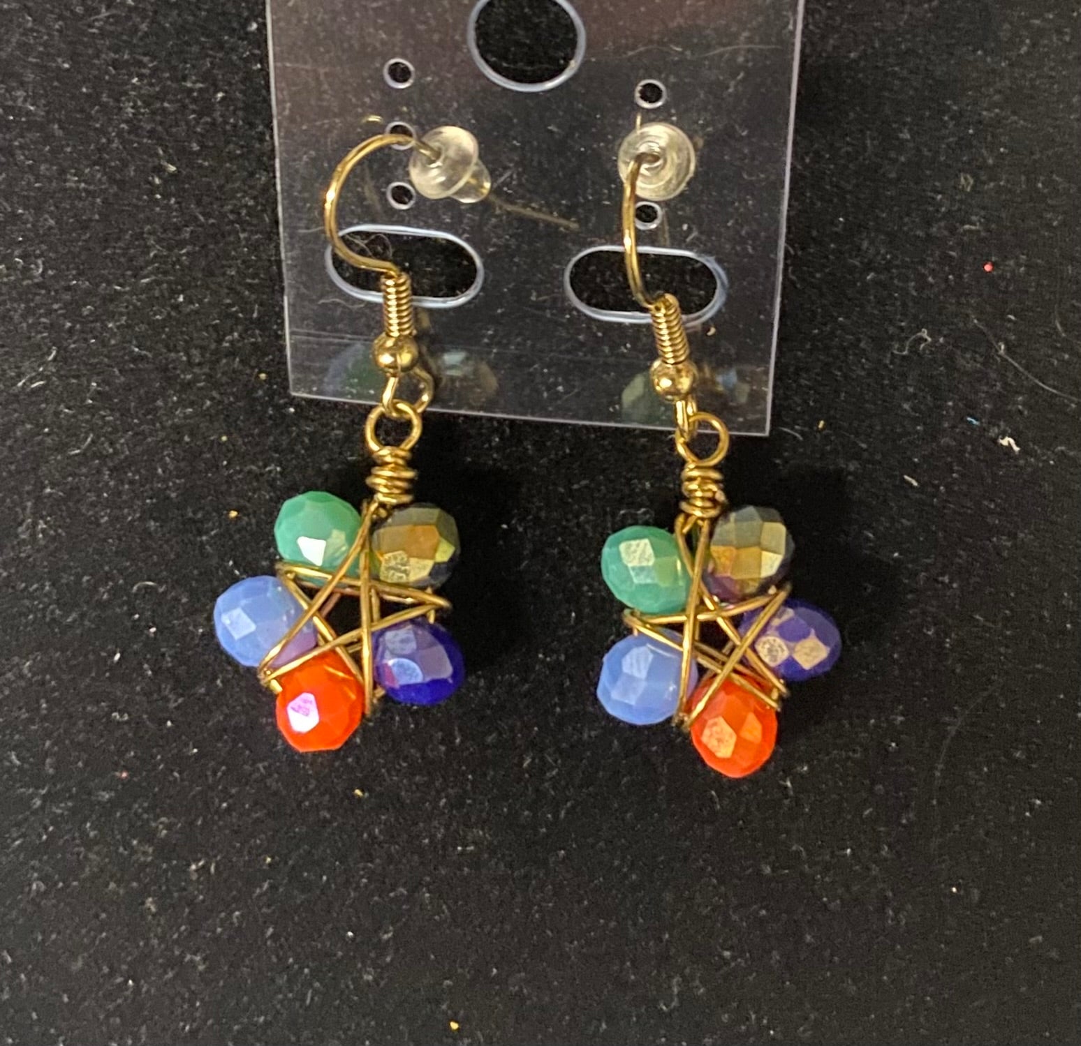 Colorful beaded earrings on a clear card against a black background