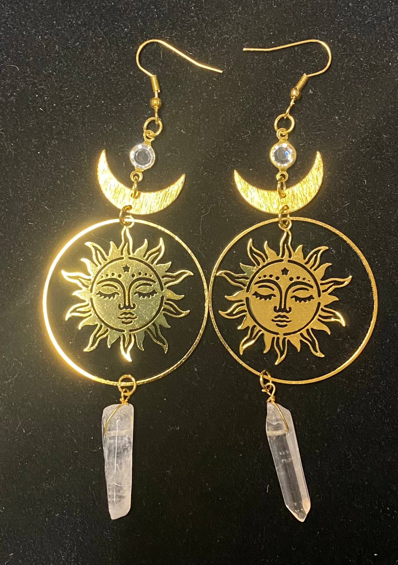 Gold sun and moon earrings with crystal pendants on a black background