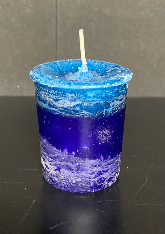Blue candle in a glass container on a black surface with a gray background