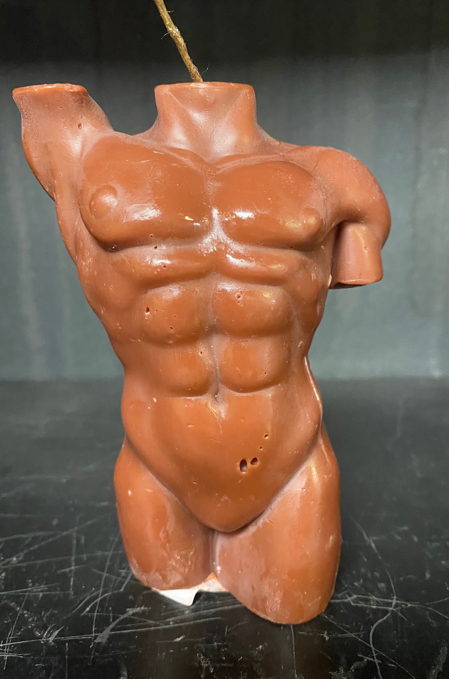 Terracotta-colored torso candle on a dark surface