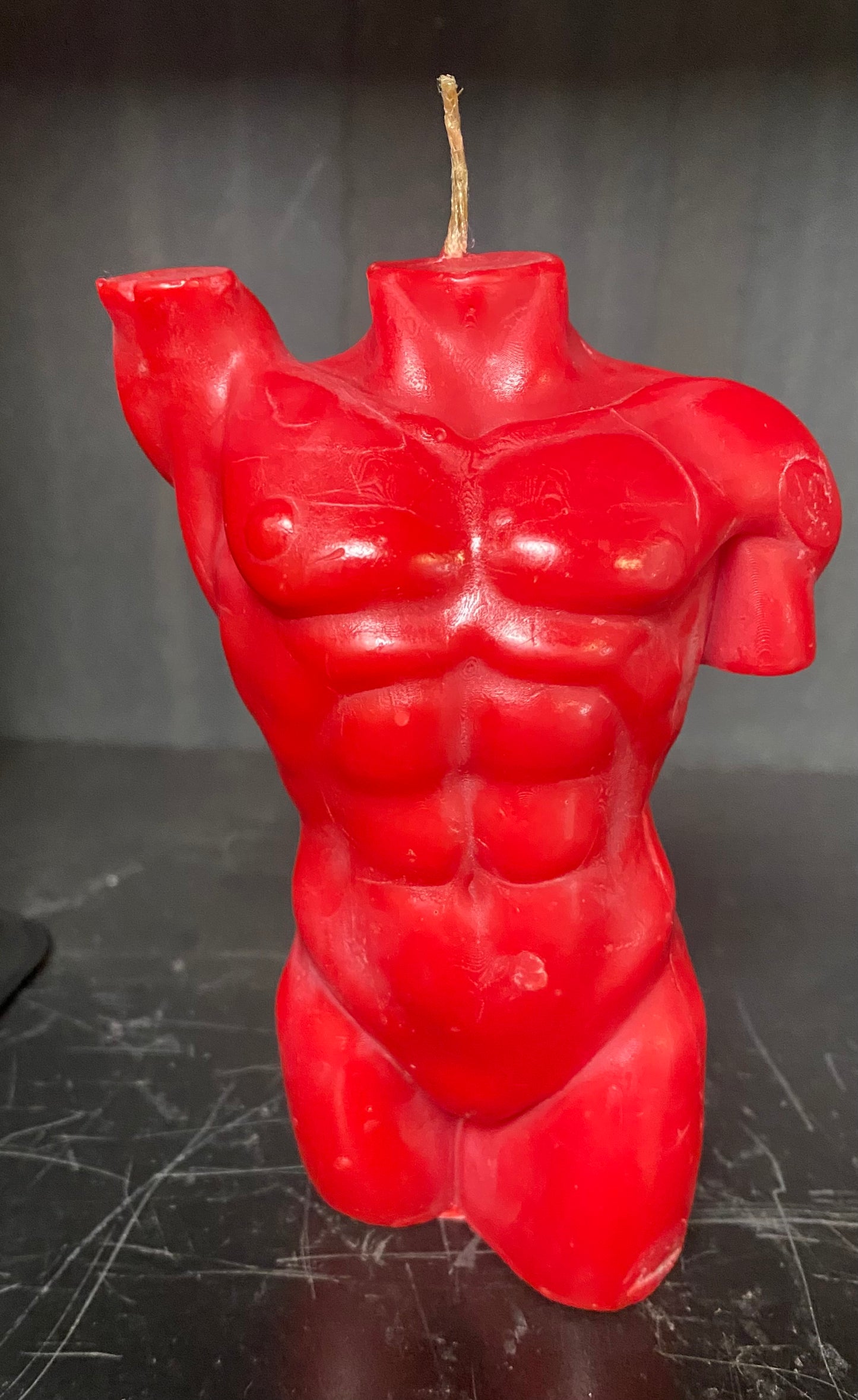 Red muscular torso candle on a dark surface