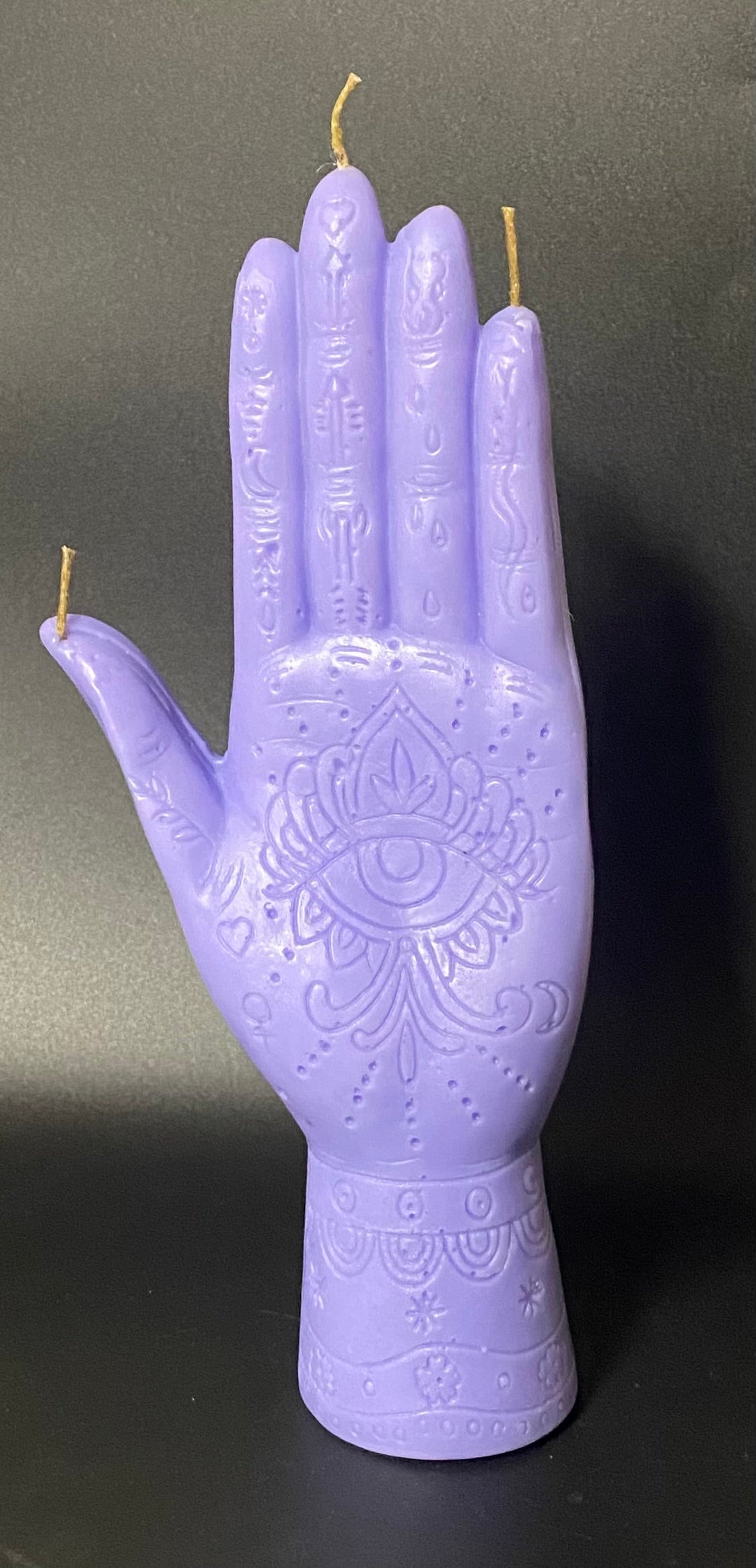 Purple hand-shaped candle with intricate designs on a dark background