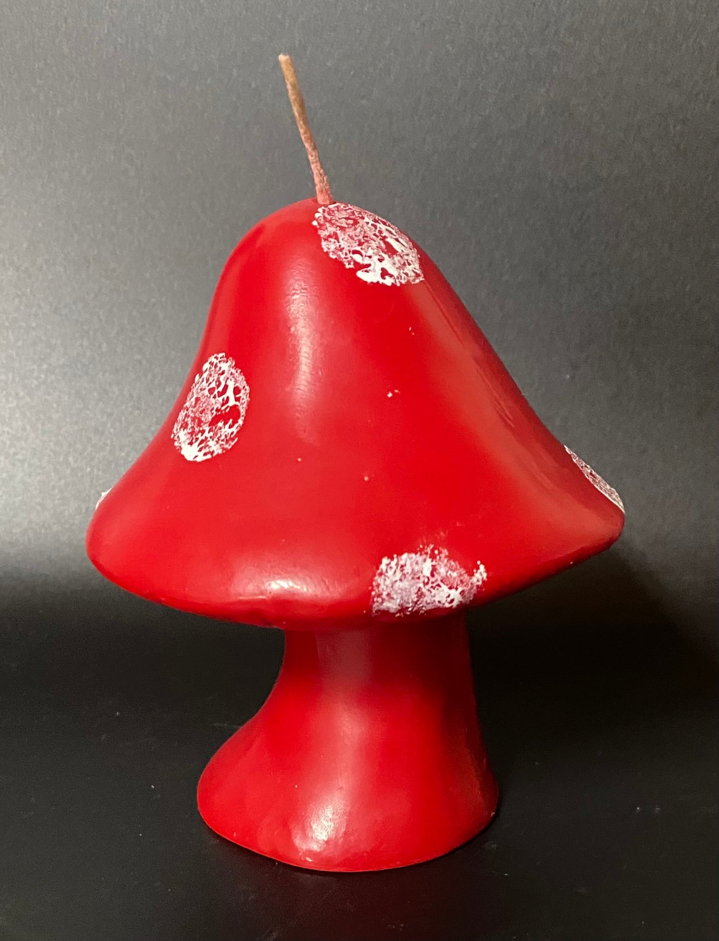 Red mushroom-shaped candle with white spots on a dark background