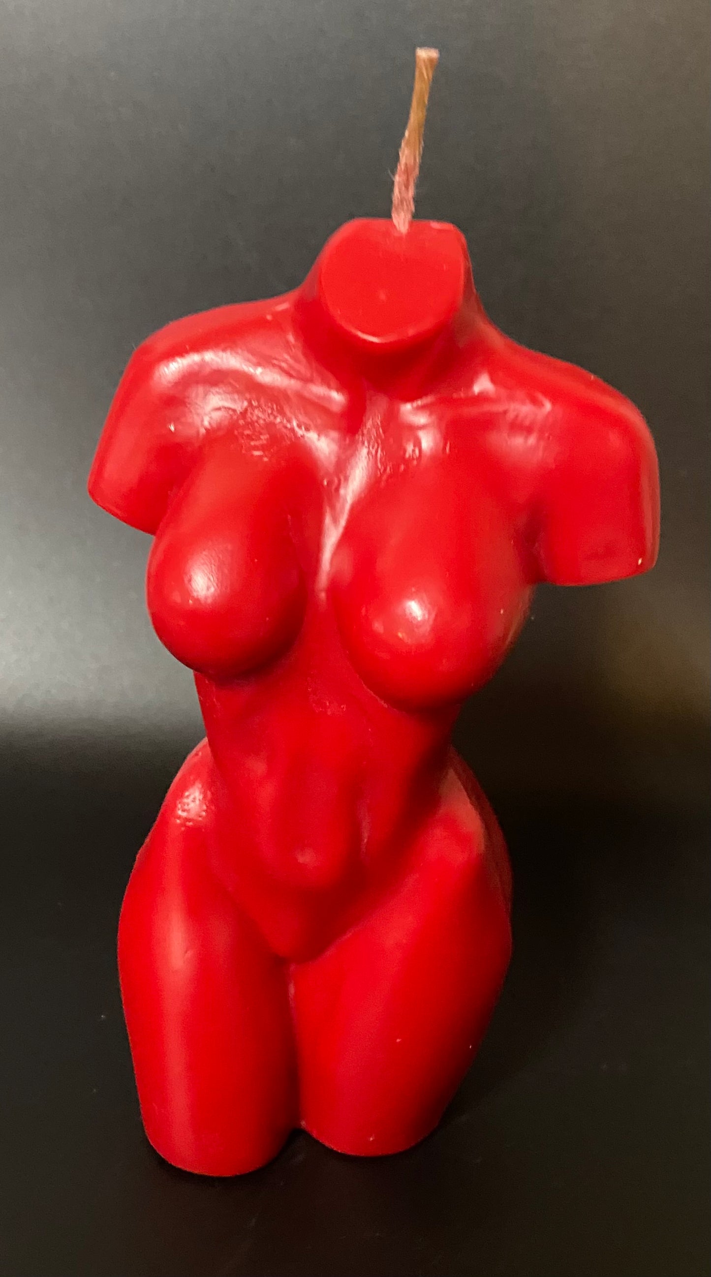 Red candle shaped like a human torso on a dark background