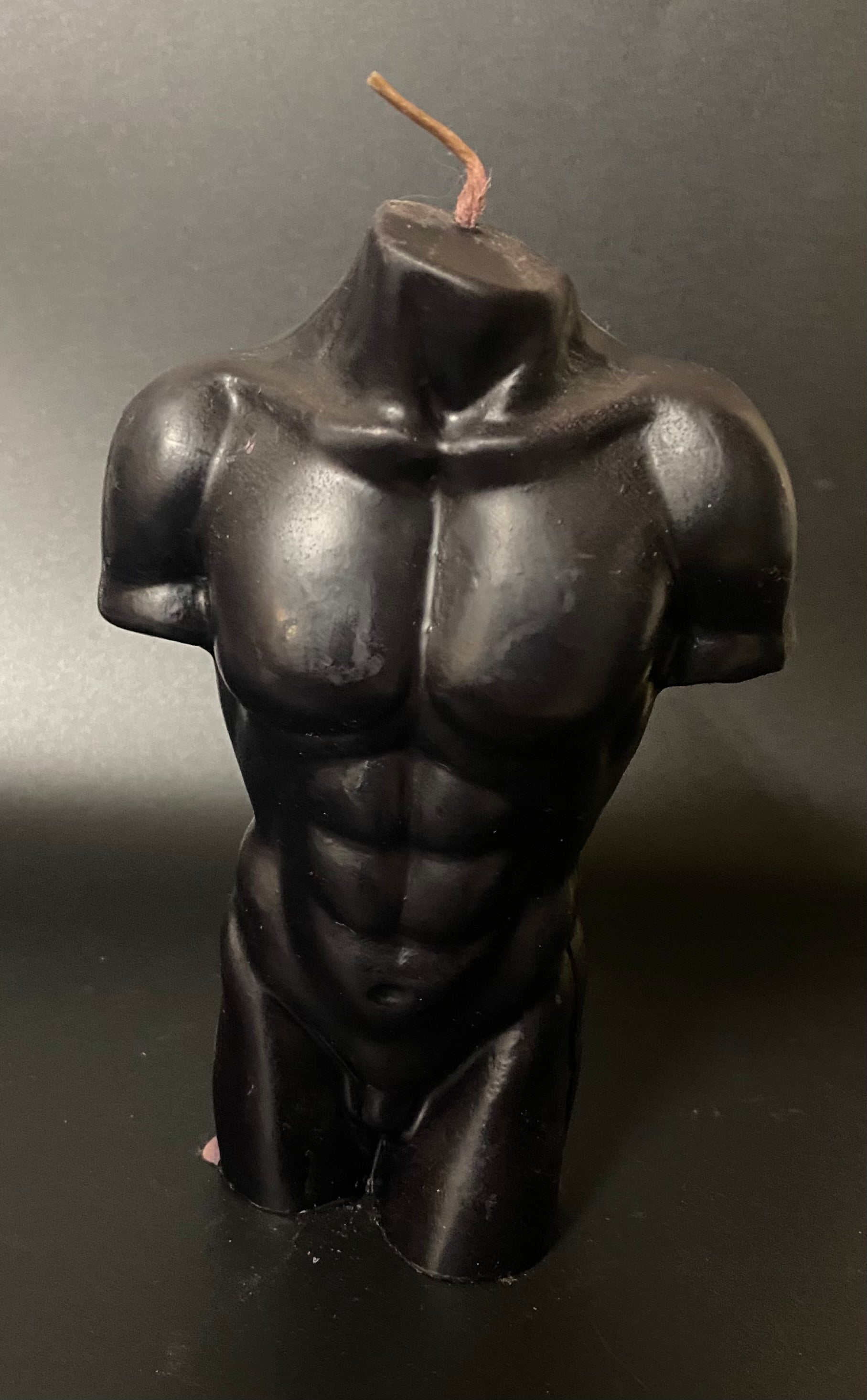 Black candle shaped like a torso on a dark background