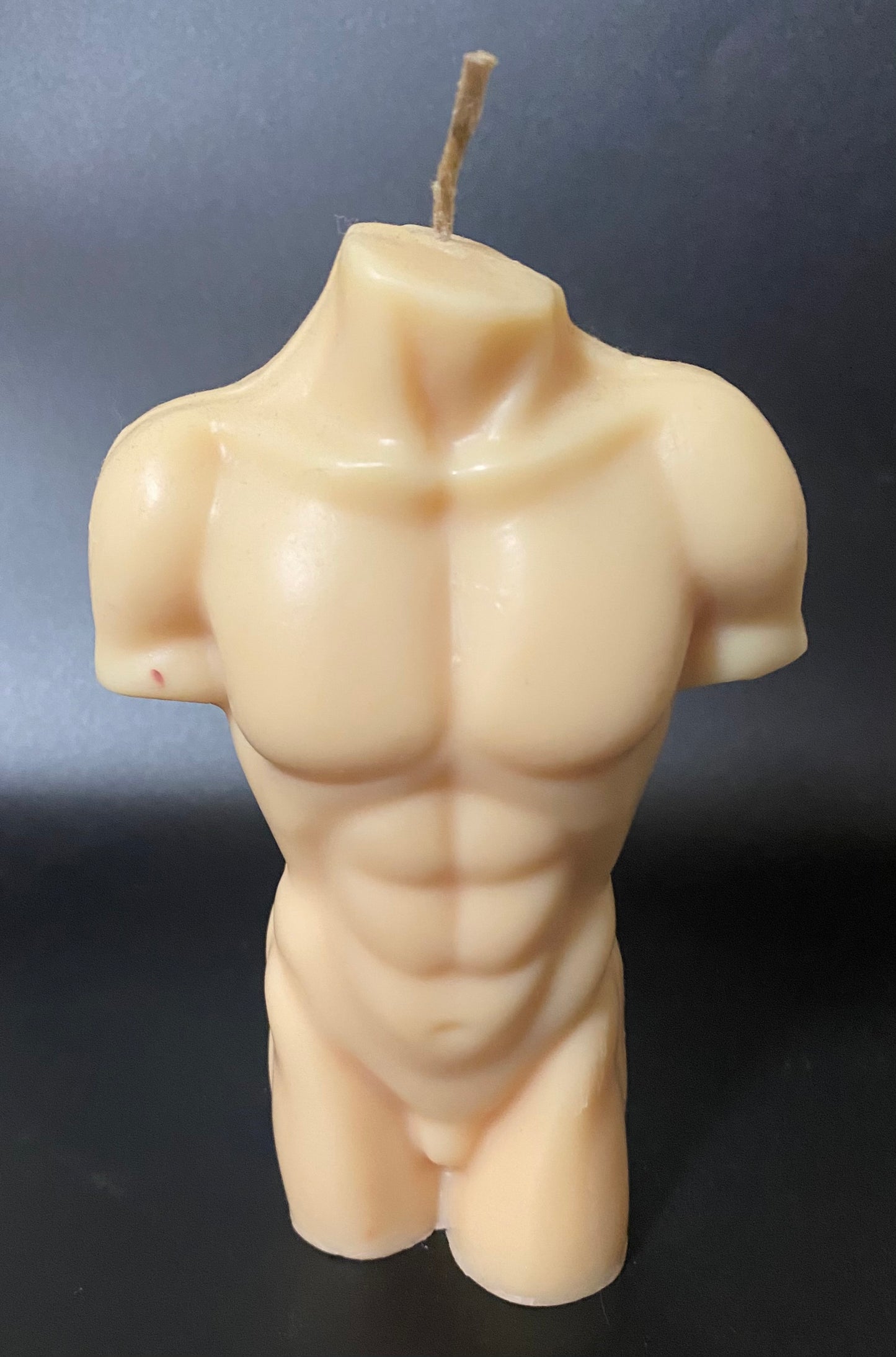 Candle shaped like a muscular torso on a dark background