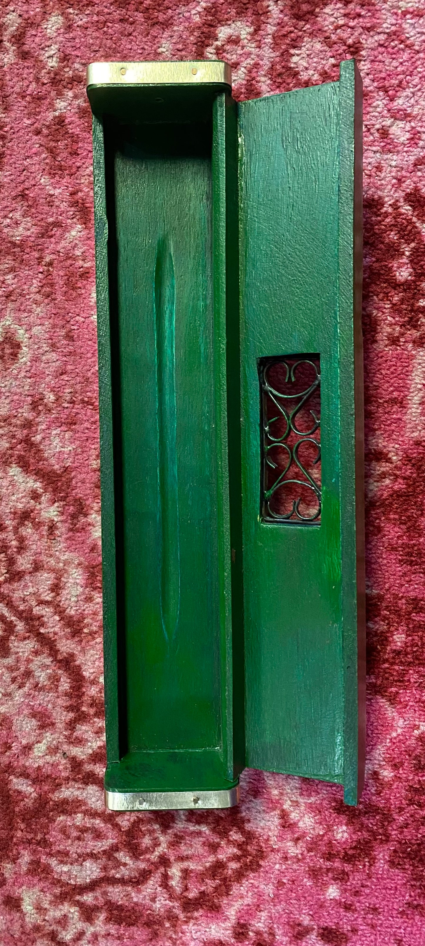 Green wooden box with a decorative panel on a red patterned fabric background