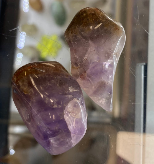 Two amethyst crystals on a reflective surface with blurred background
