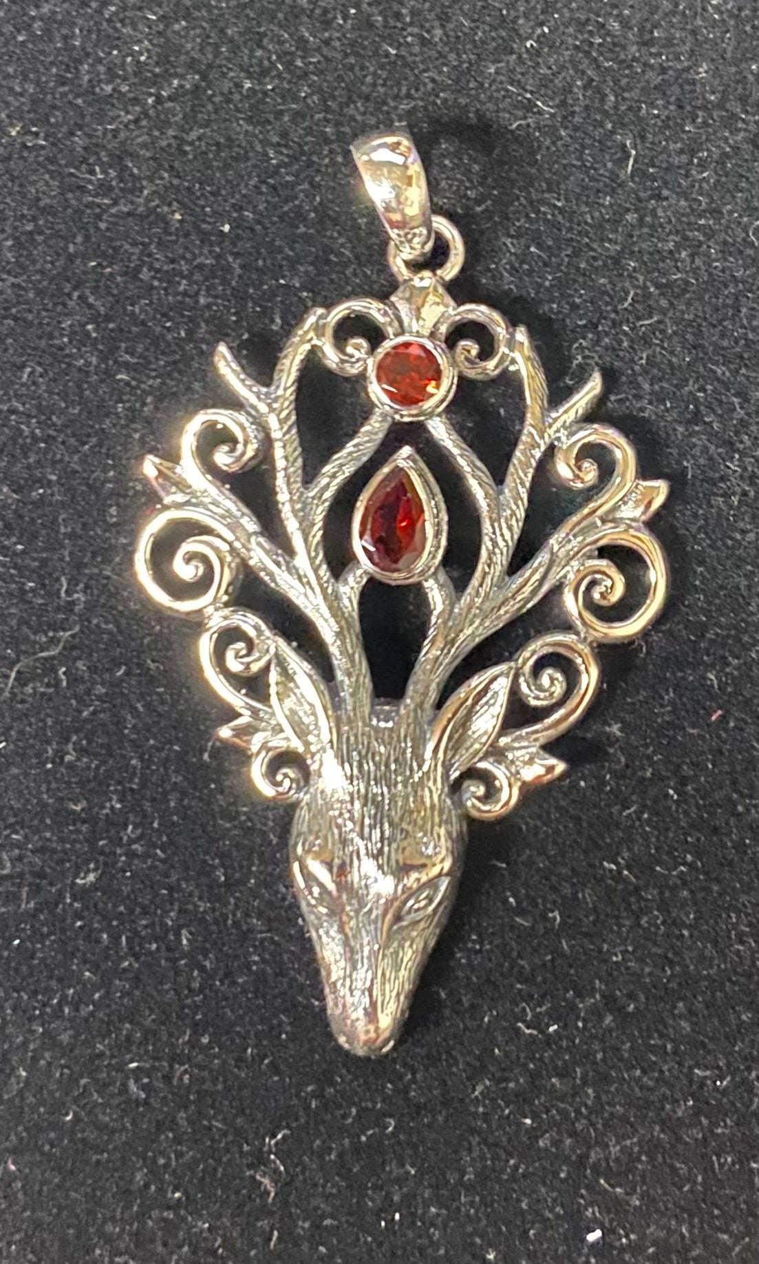 Silver pendant with deer head design and red stones on a black background