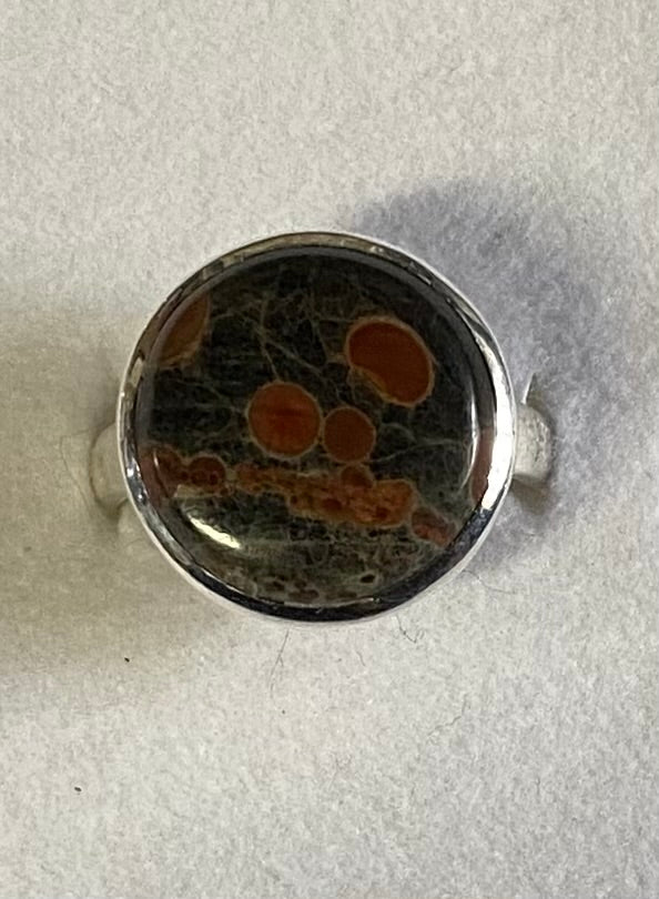 Silver ring with a circular design featuring black and orange patterns on a light gray background
