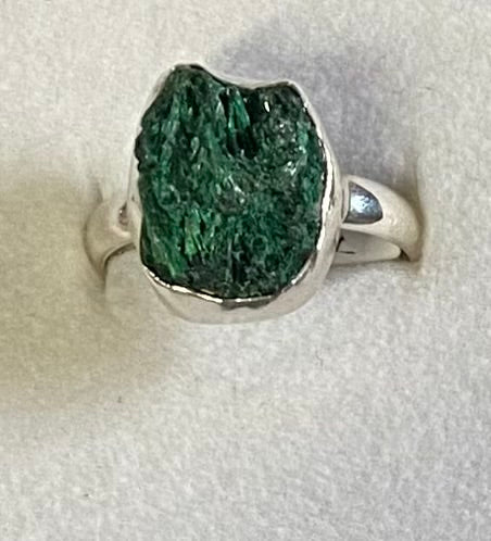 Silver ring with a large green mineral stone on a light gray background