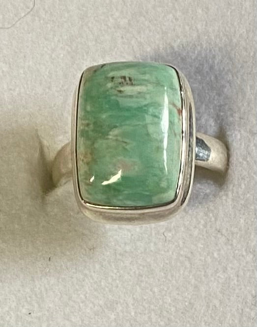 Ring with a green stone and silver band on a light gray background