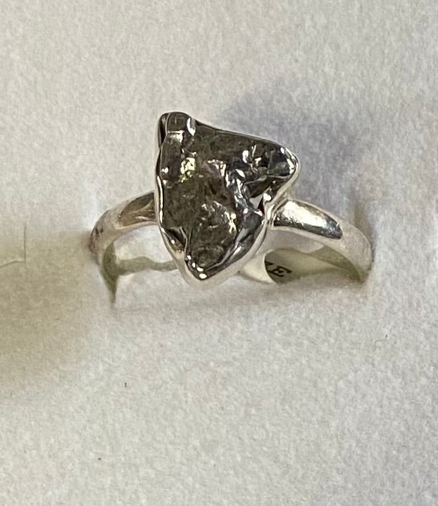 Silver ring with a large, rough-cut gemstone on a light gray background
