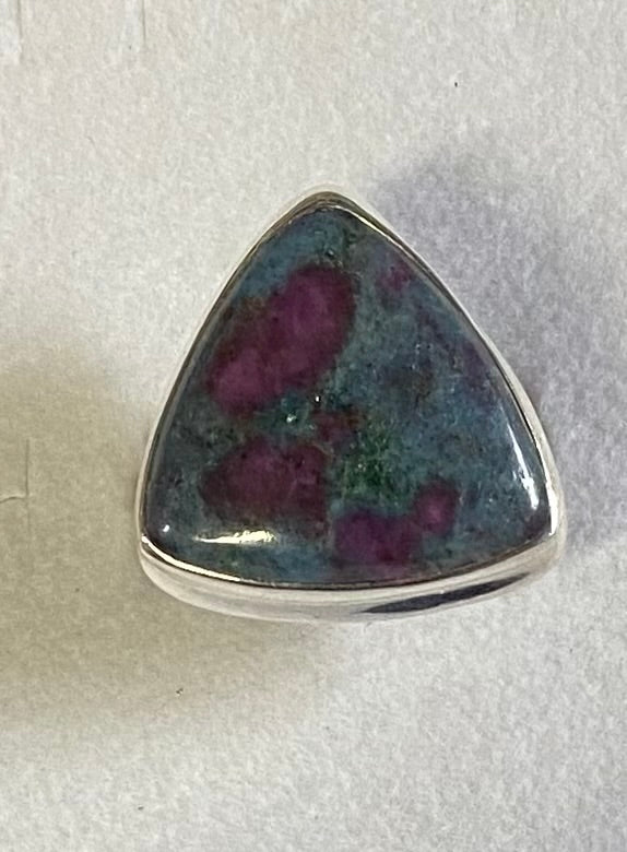 Triangular gemstone with purple and green inclusions in a silver setting on a light gray background