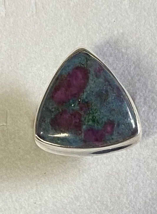 Triangular gemstone with purple and green inclusions in a silver setting on a light gray background