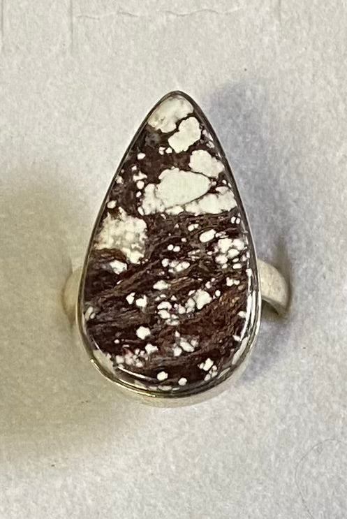 Teardrop-shaped ring with brown and white speckled stone on a light gray background