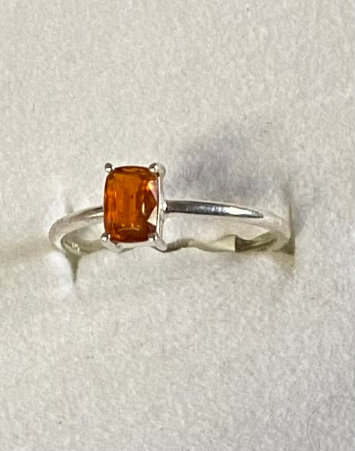 Silver ring with a rectangular orange gemstone on a light gray background