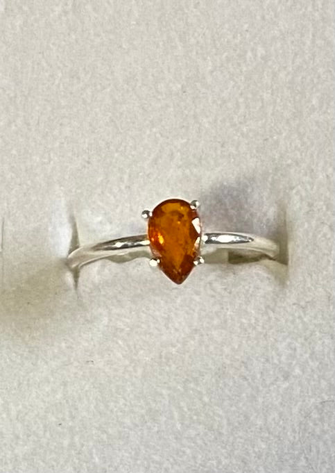 Silver ring with a pear-shaped orange gemstone on a light gray background