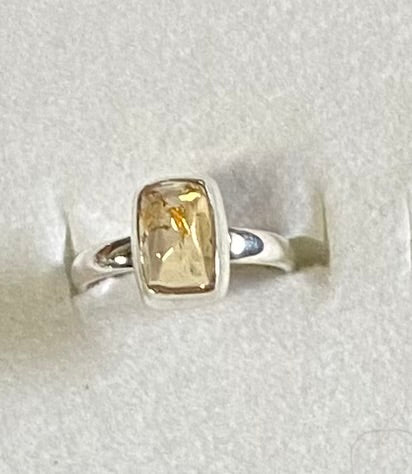 Silver ring with a rectangular yellow gemstone on a light gray background