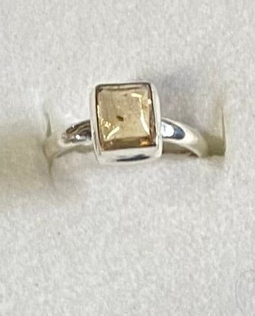 Silver ring with a square-cut gemstone on a light gray background