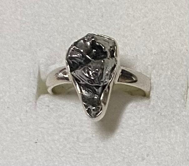 Silver ring with a large, rough-cut gemstone on a light gray background