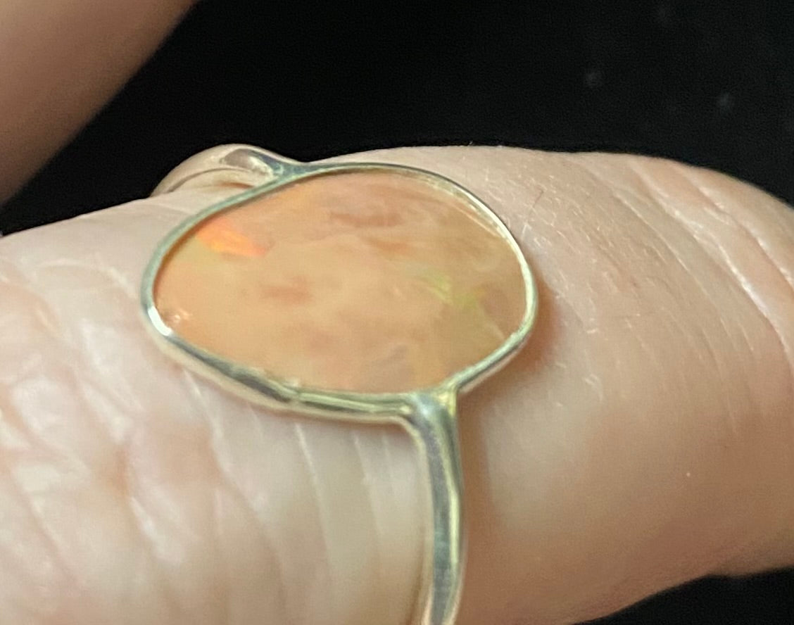 Opal ring on a finger with a dark background