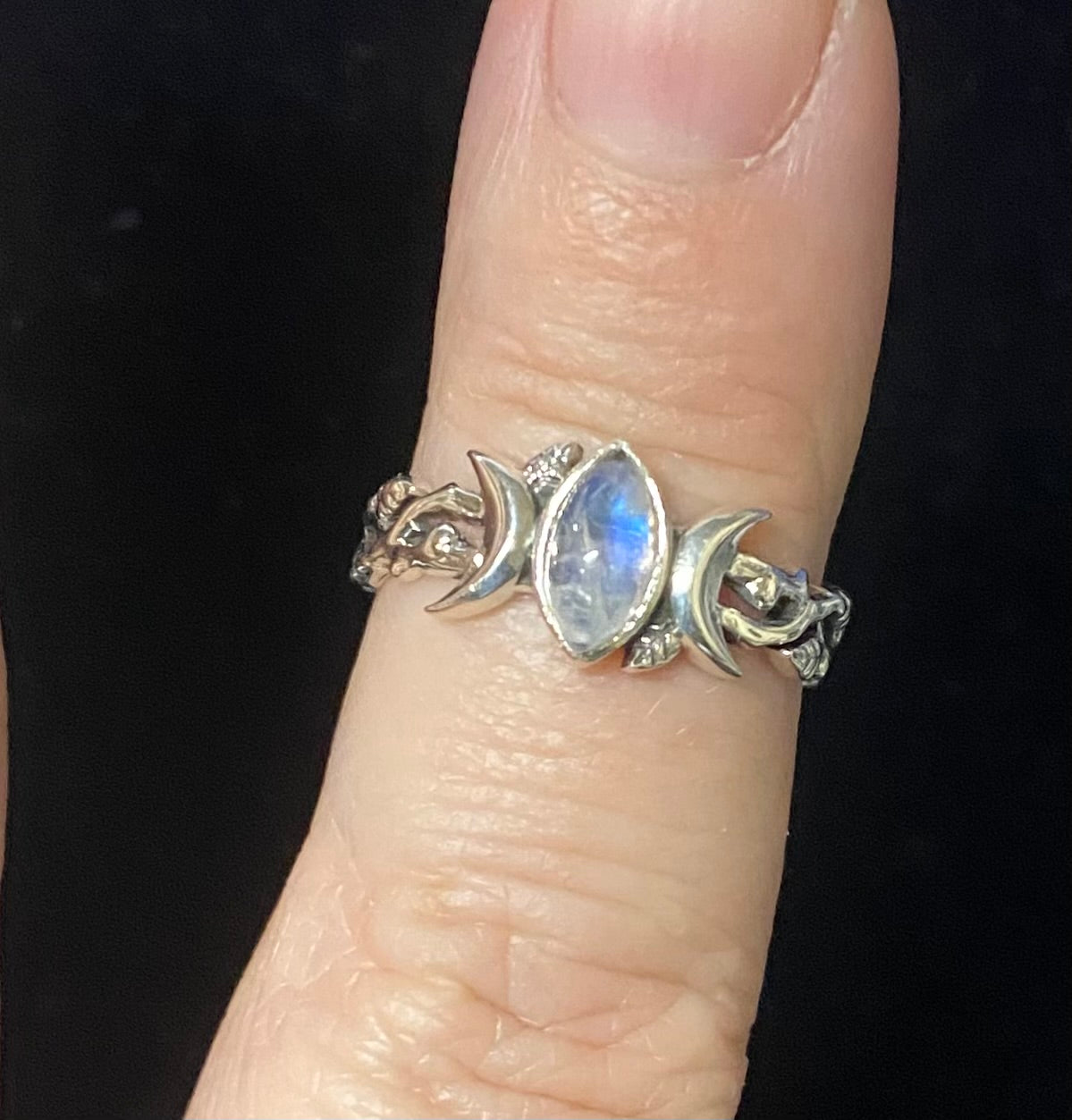Silver ring with a central gemstone on a finger against a black background