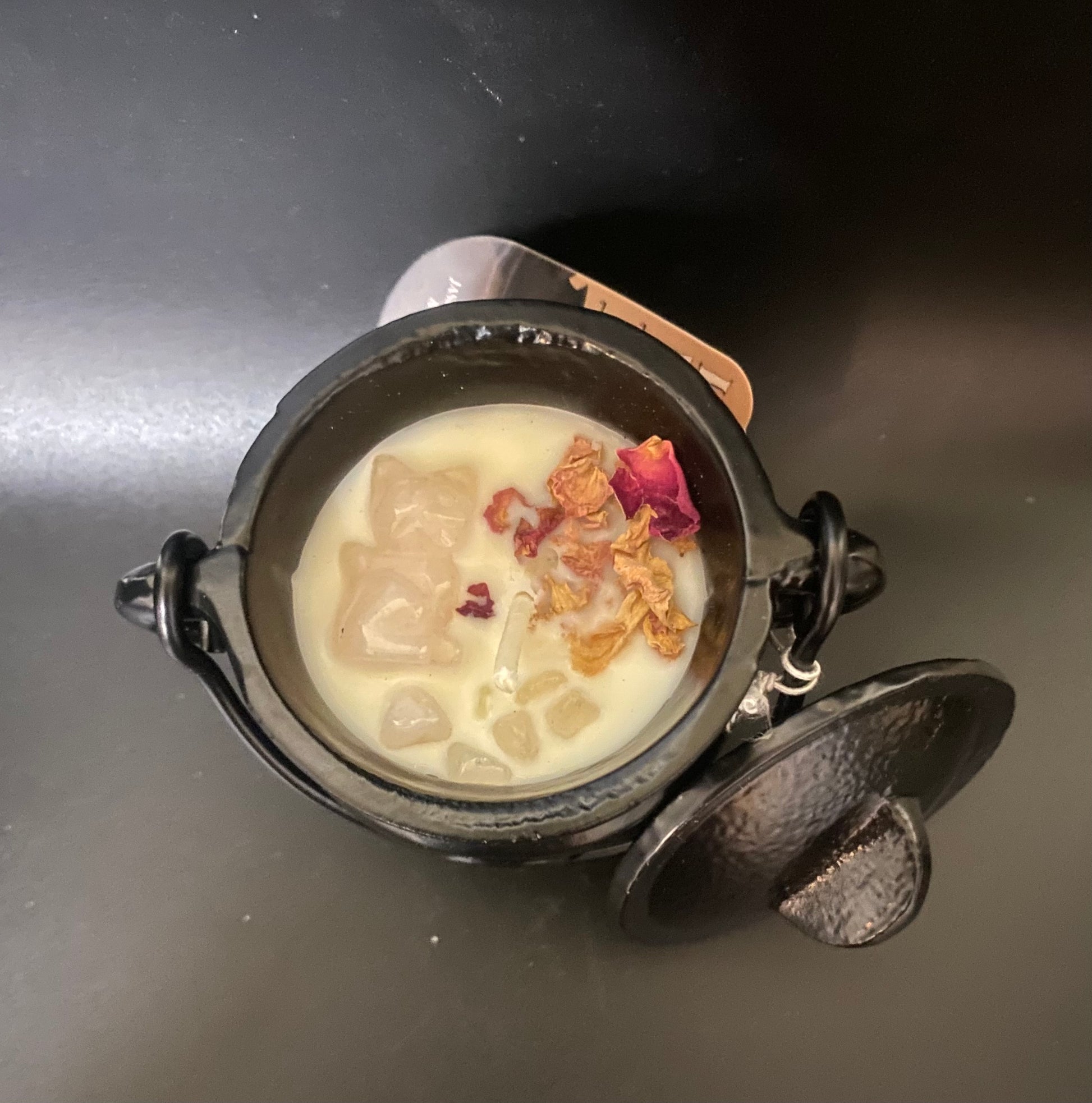 Small black cauldron candle and dried flowers on a dark surface