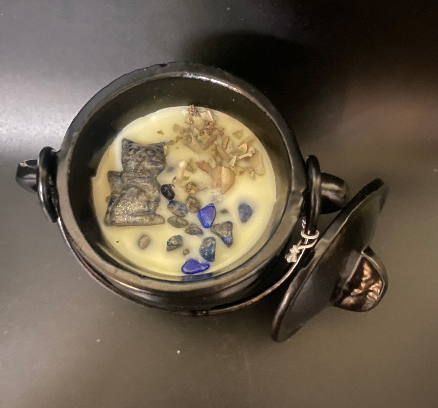 Decorative cauldron candle with stones and a small figurine on a dark surface