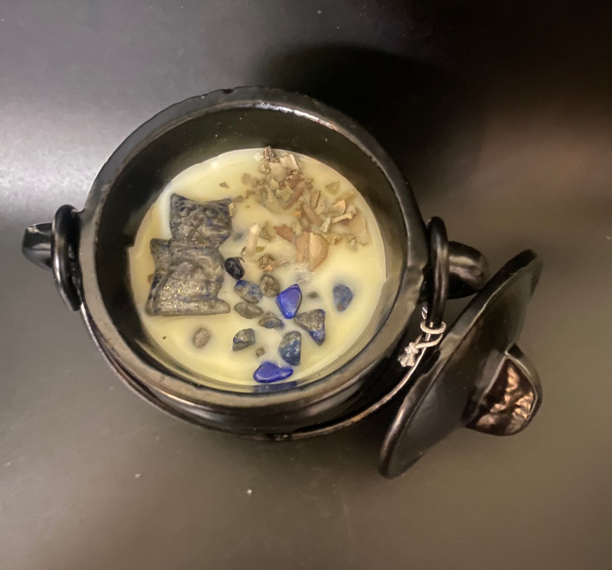 Decorative cauldron candle with stones and a small figurine on a dark surface