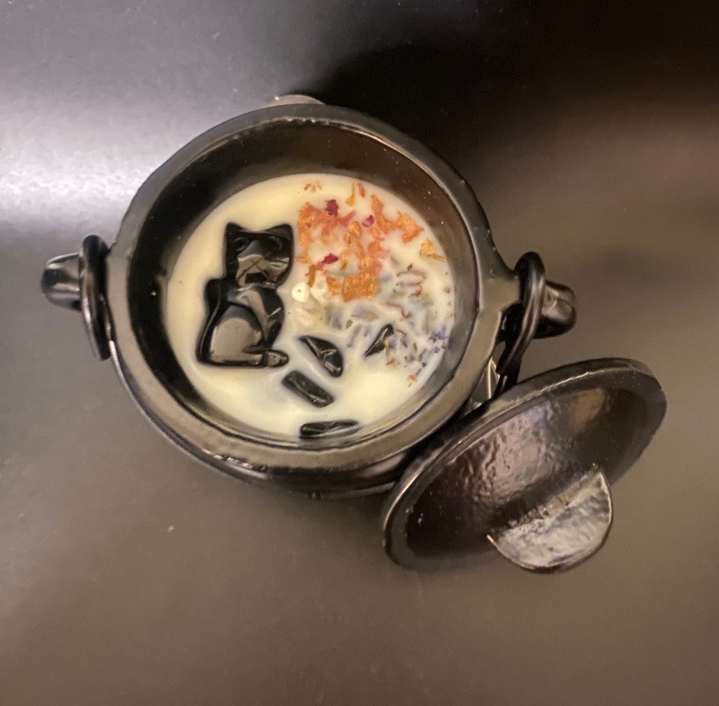 Cauldron candle with a cat in obsidian on a dark surface