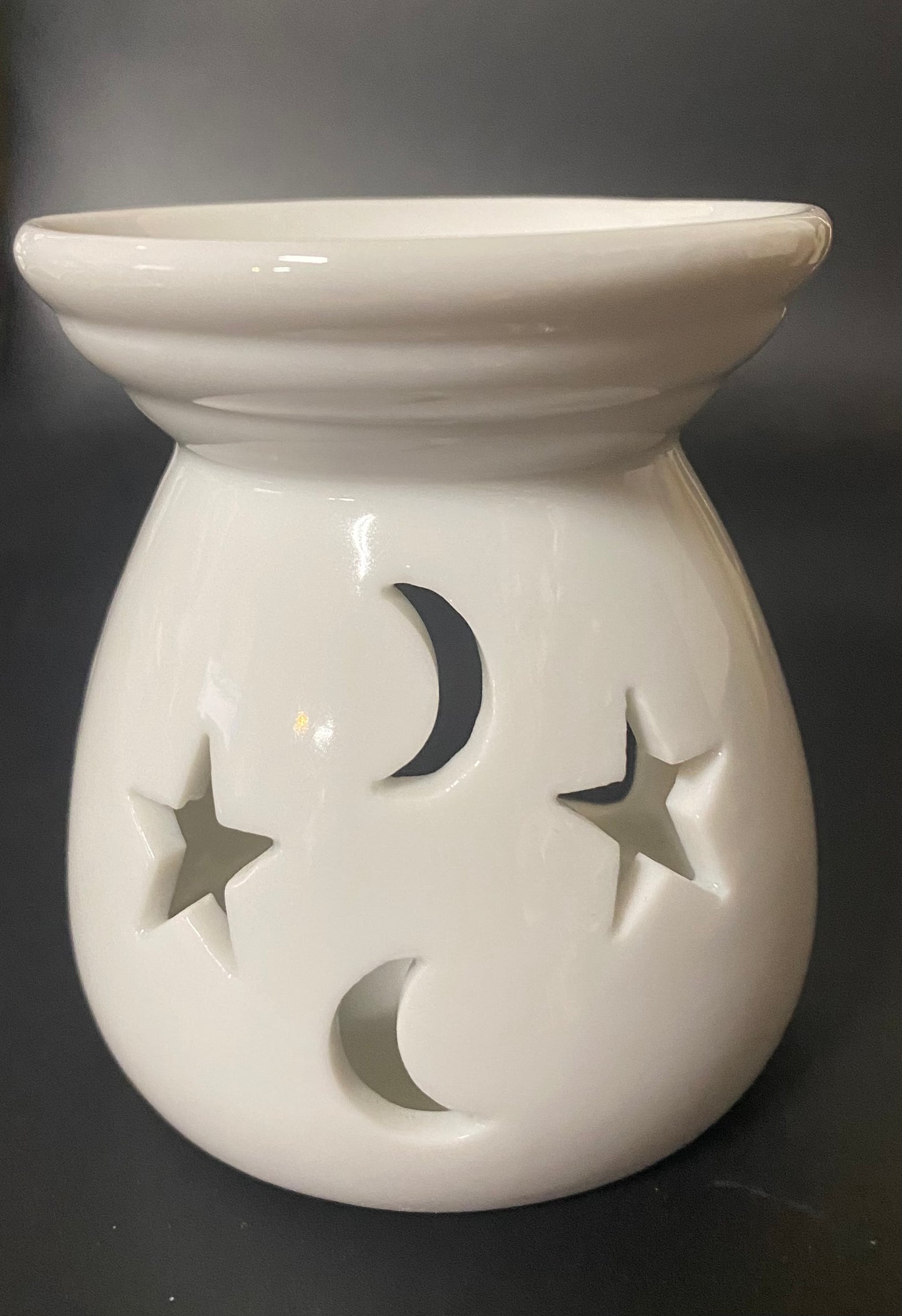 White ceramic warmer with star and moon cutouts on a black background