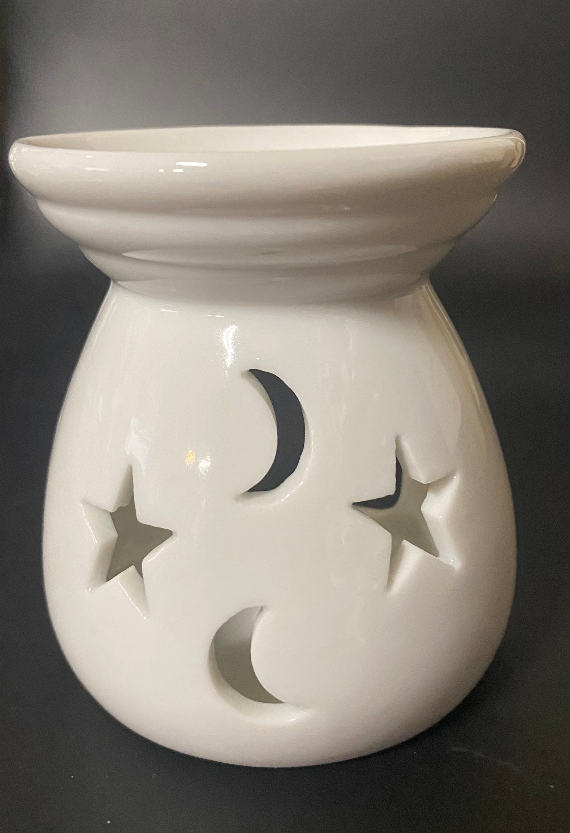 White ceramic warmer with star and moon cutouts on a black background
