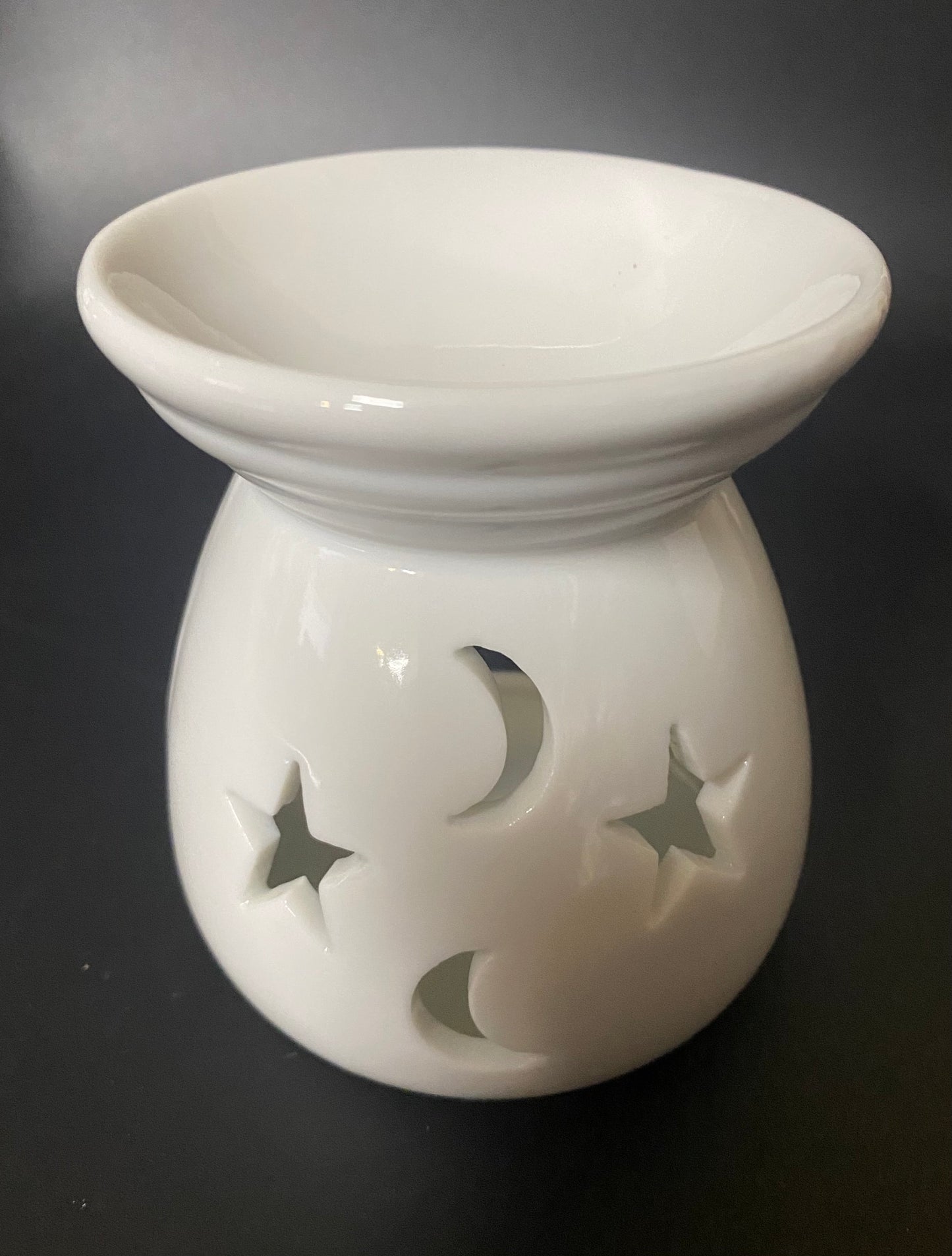 White ceramic oil burner with star and moon designs on a black background
