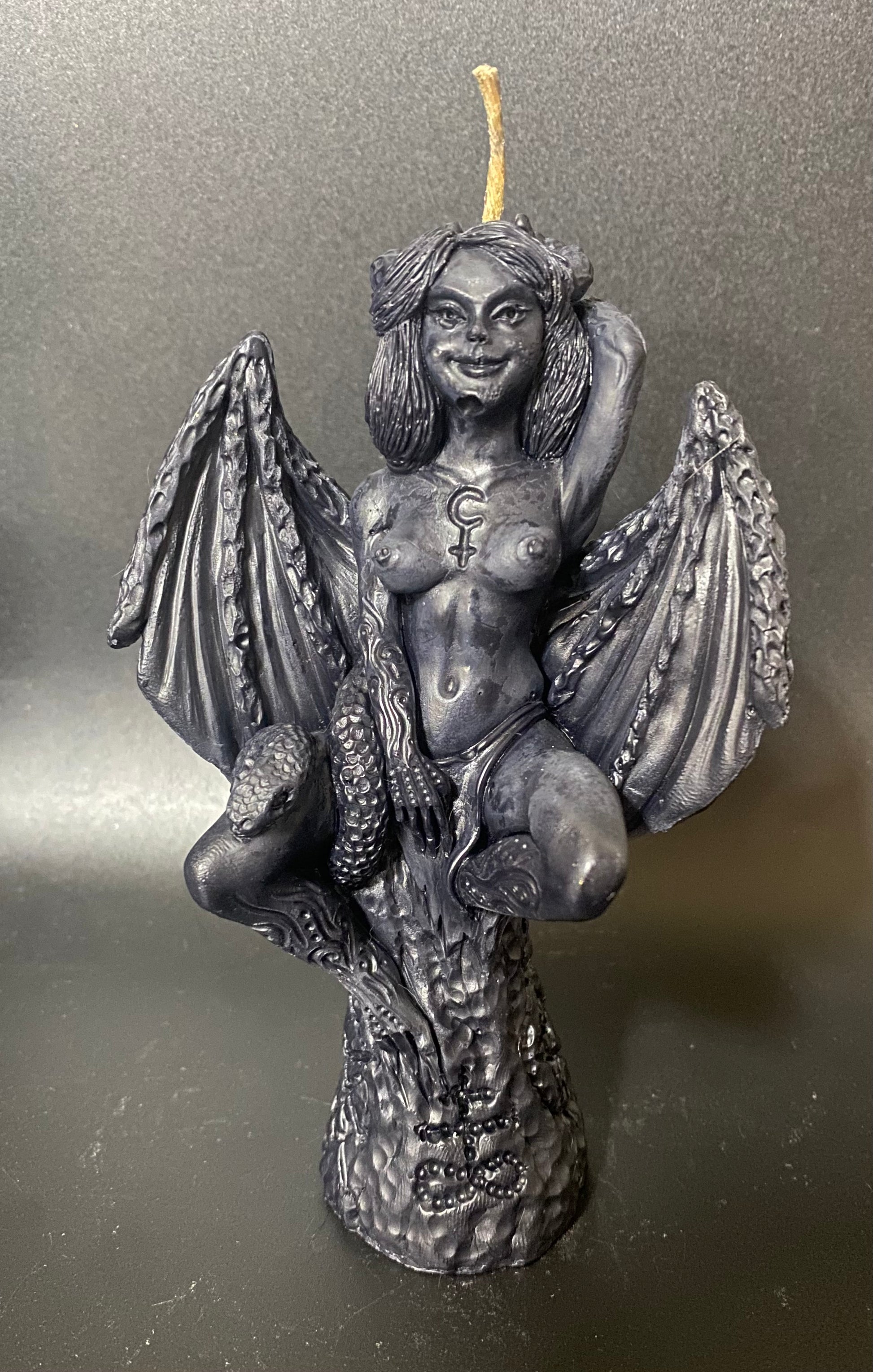 Candle in the shape of a winged creature with a candle on a gray background
