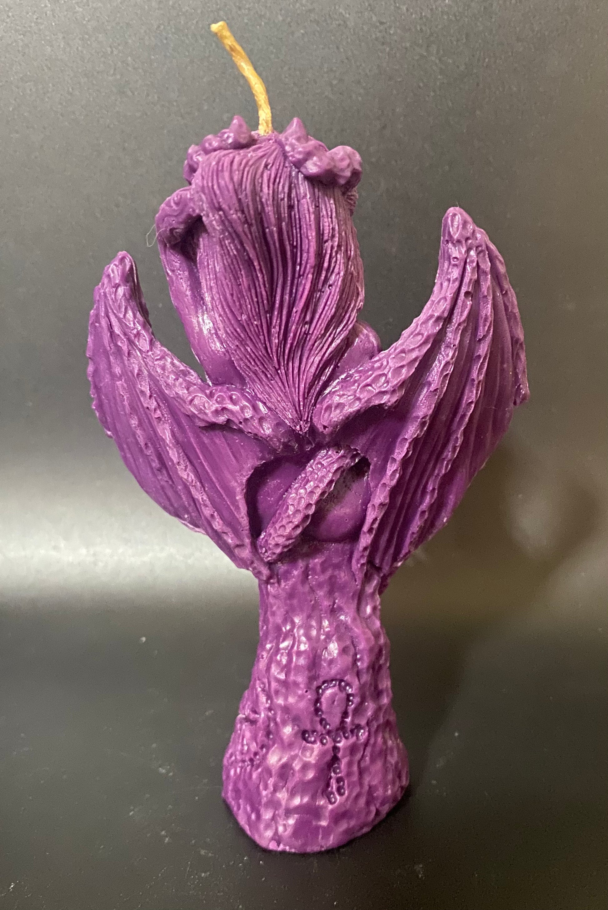 Purple candle shaped like a Lilith back on a reflective surface