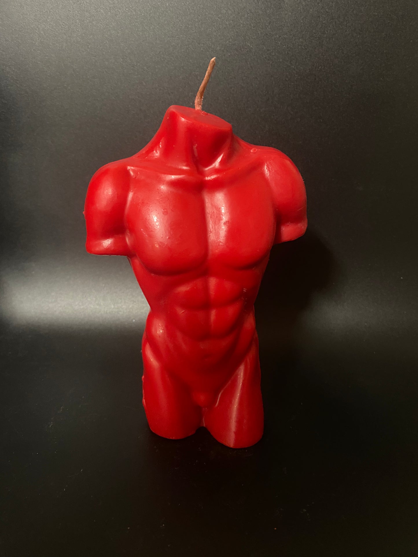 Red muscular torso candle on a black background
