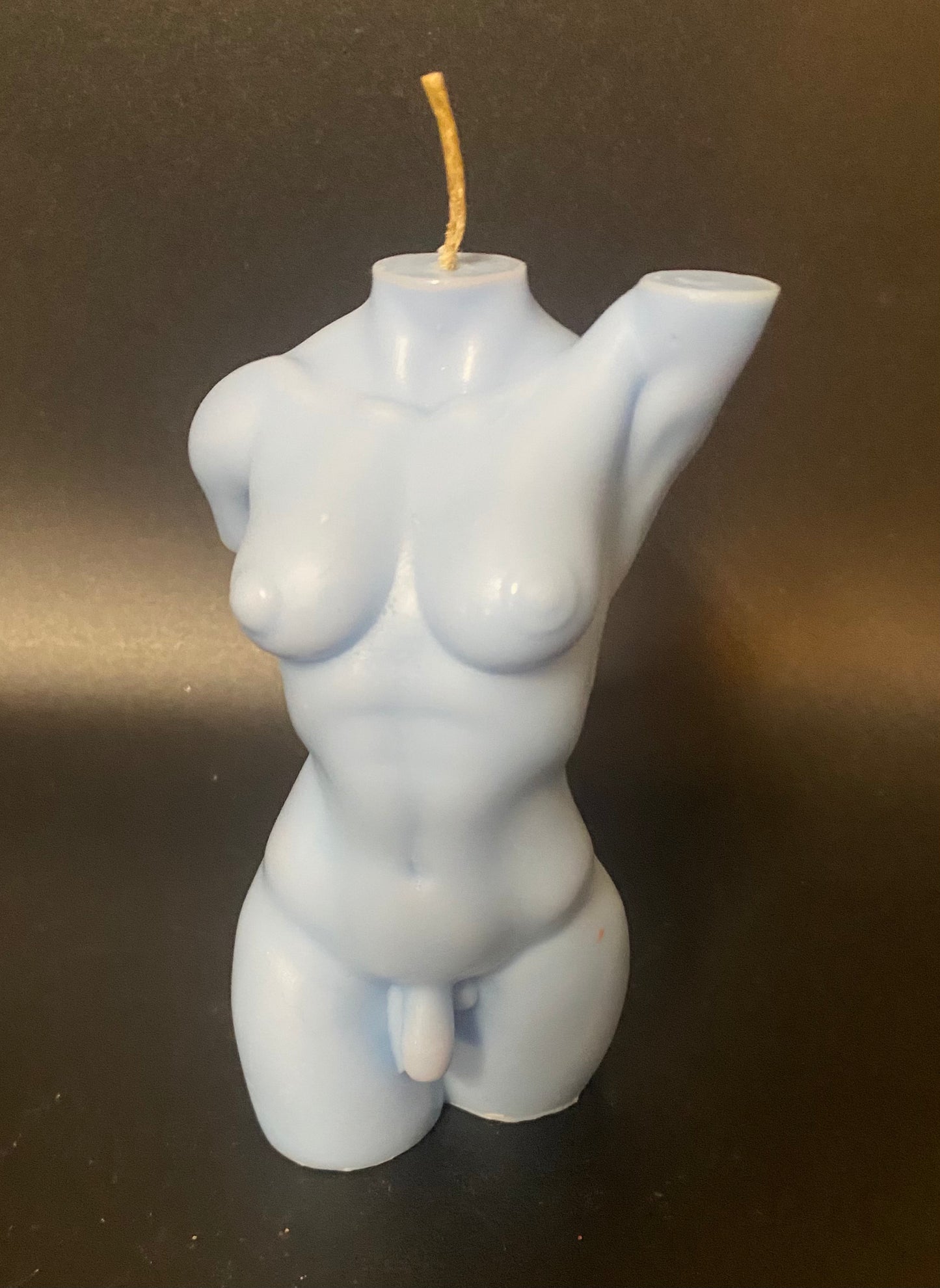 Candle shaped like a torso on a dark surface