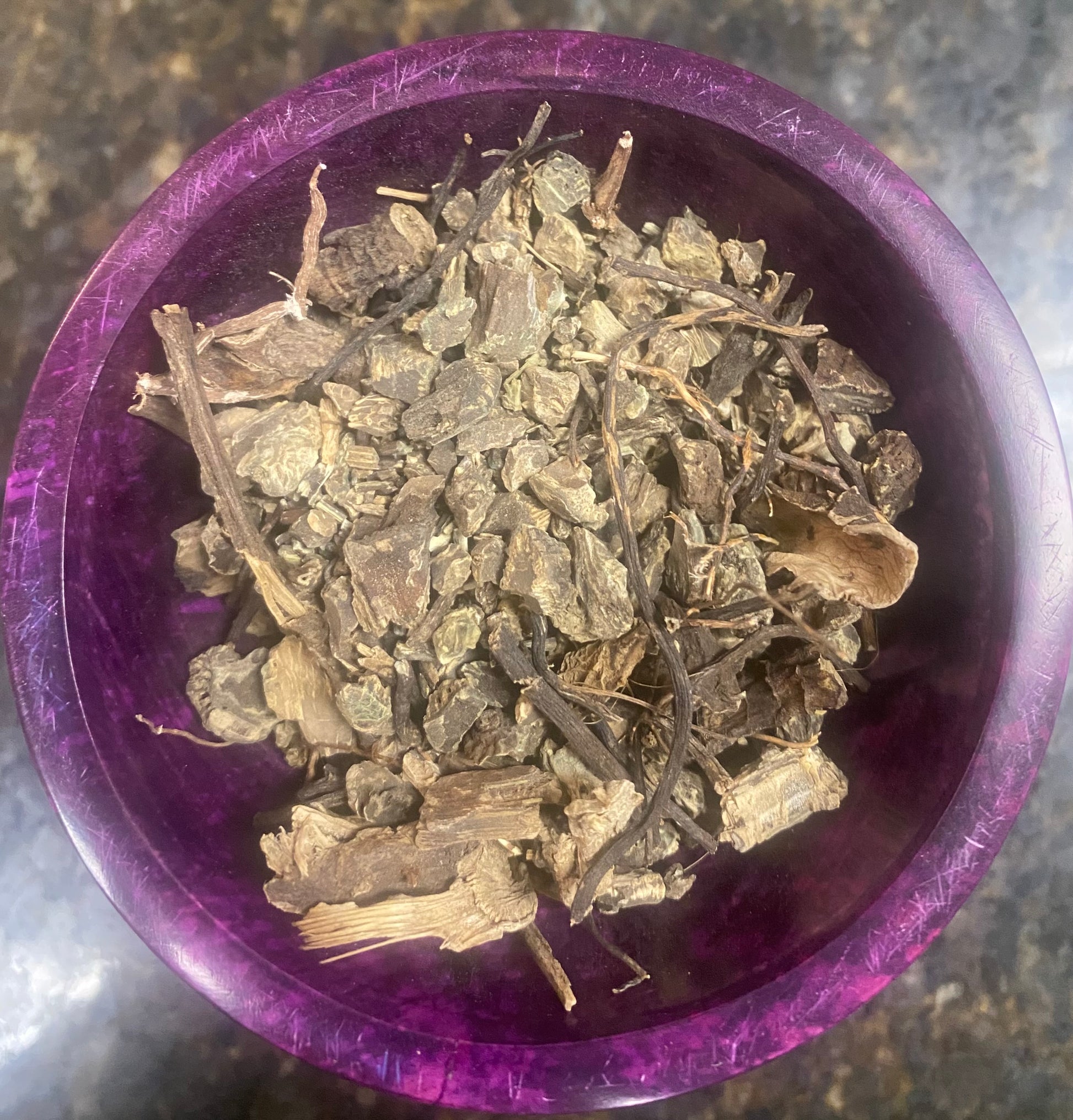 Purple container filled with dried herbs on a textured surface
