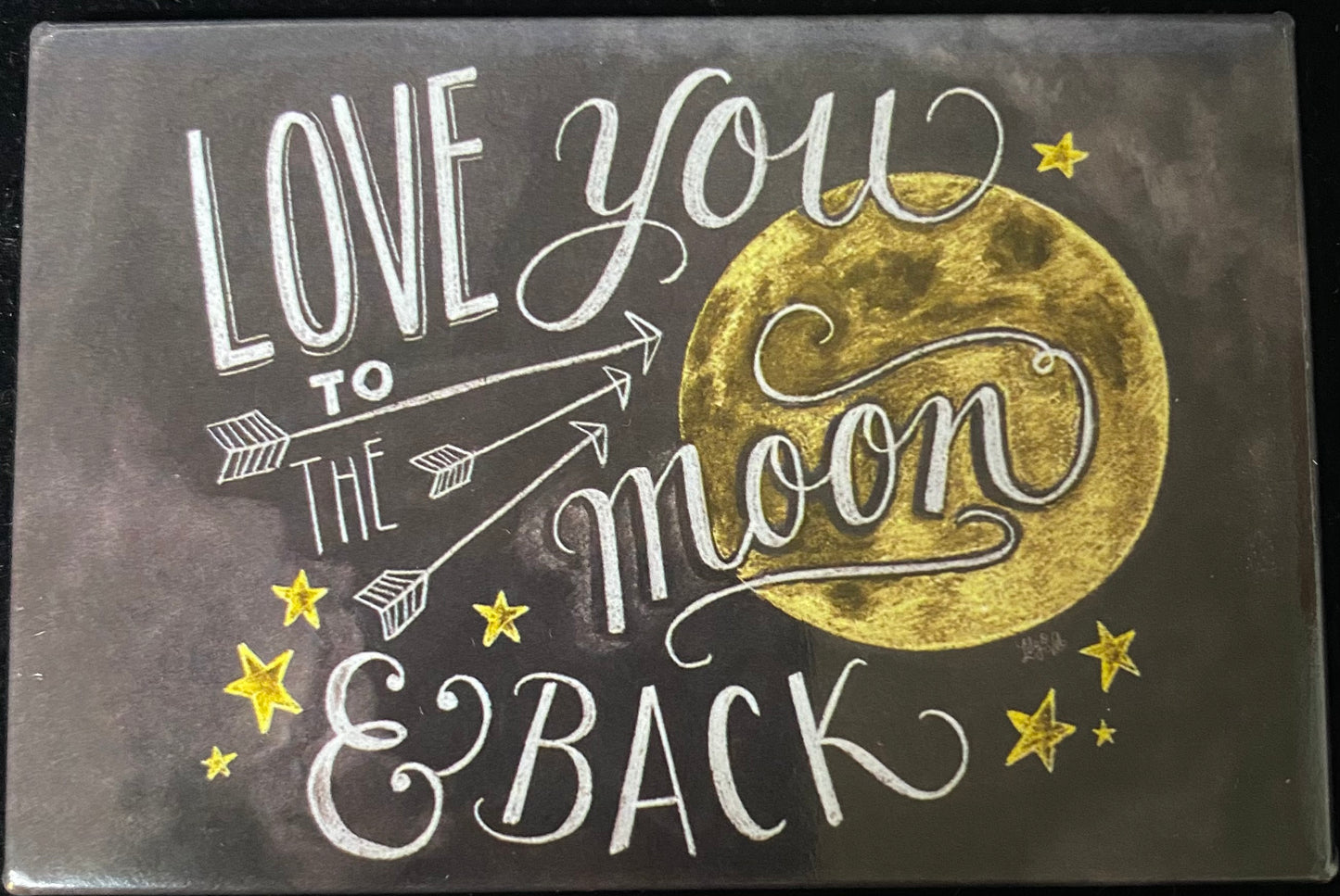 A square decorative magnet with a dark charcoal background featuring the phrase 'LOVE YOU TO THE moon & BACK' in white script and block lettering, alongside a large textured gold moon and small gold stars.
