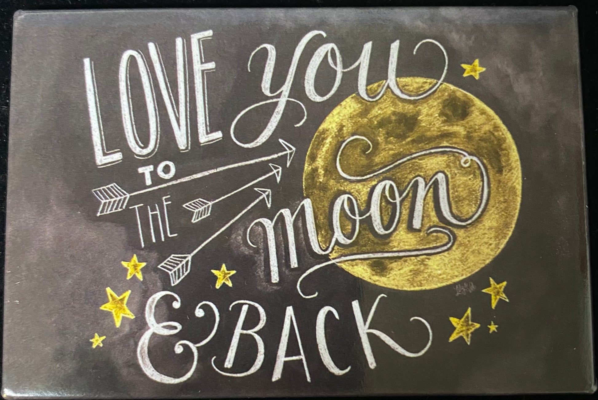 A square decorative magnet with a dark charcoal background featuring the phrase 'LOVE YOU TO THE moon & BACK' in white script and block lettering, alongside a large textured gold moon and small gold stars.