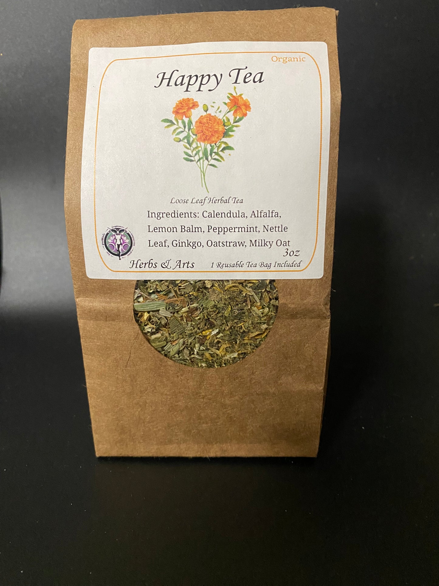 A 3 oz kraft paper tea bag package for Happy Tea Organic herbal tea, featuring a circular cutout window showing the loose herbal blend inside, set against a dark background.