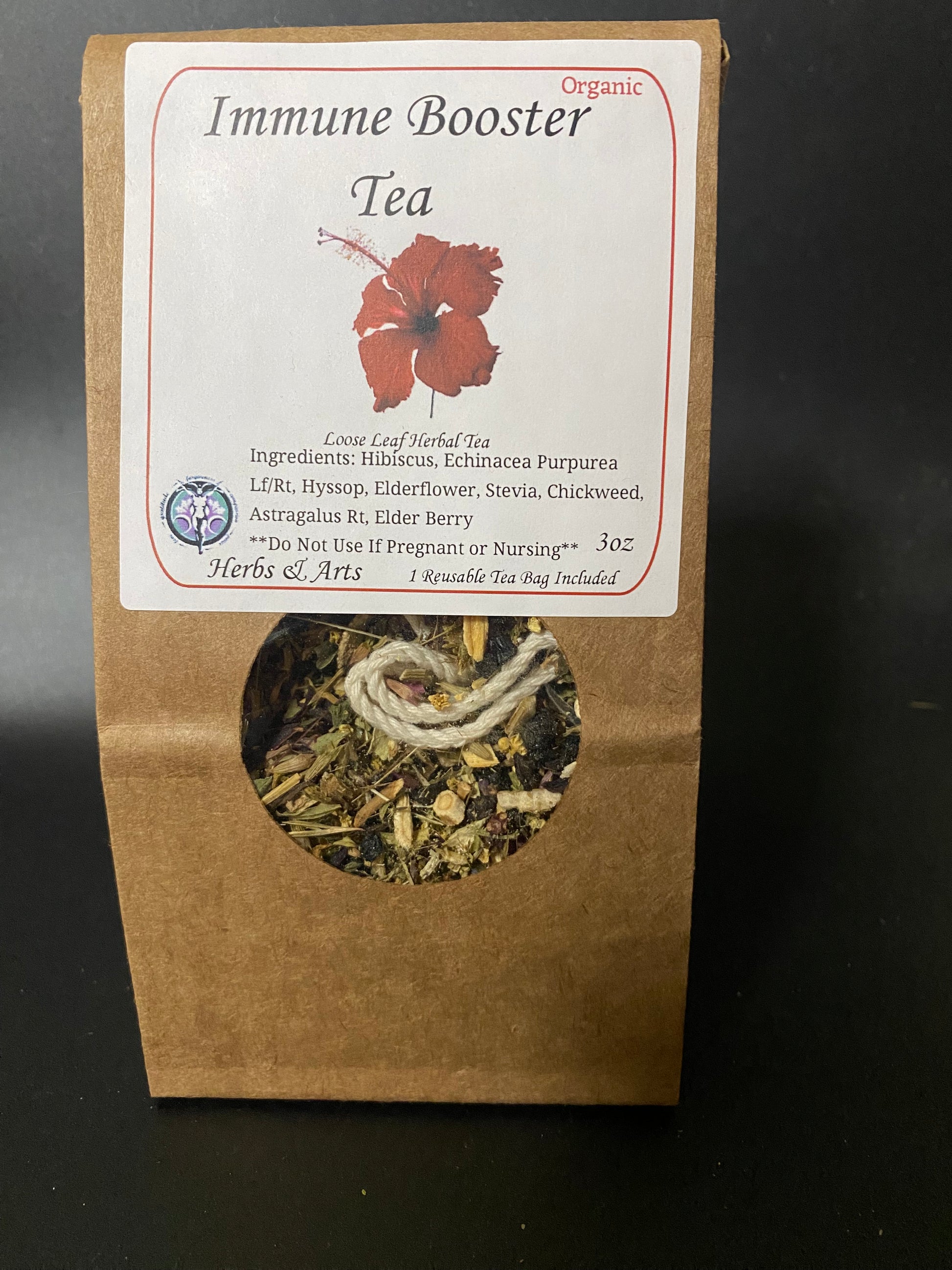 A stand-up kraft paper pouch of Immune Booster Tea with a white label and a circular window showing the dried herbal tea inside, photographed against a dark background.