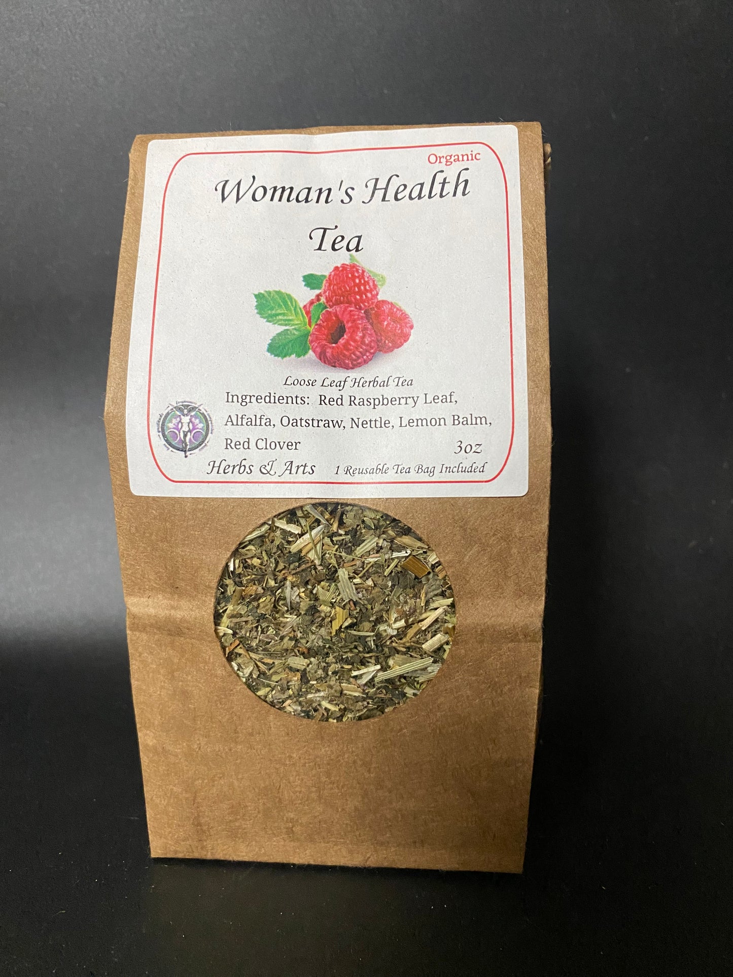 A stand-up kraft paper pouch of Woman's Health Tea with a white label and a circular window showing loose leaf herbal tea inside, photographed against a dark background.