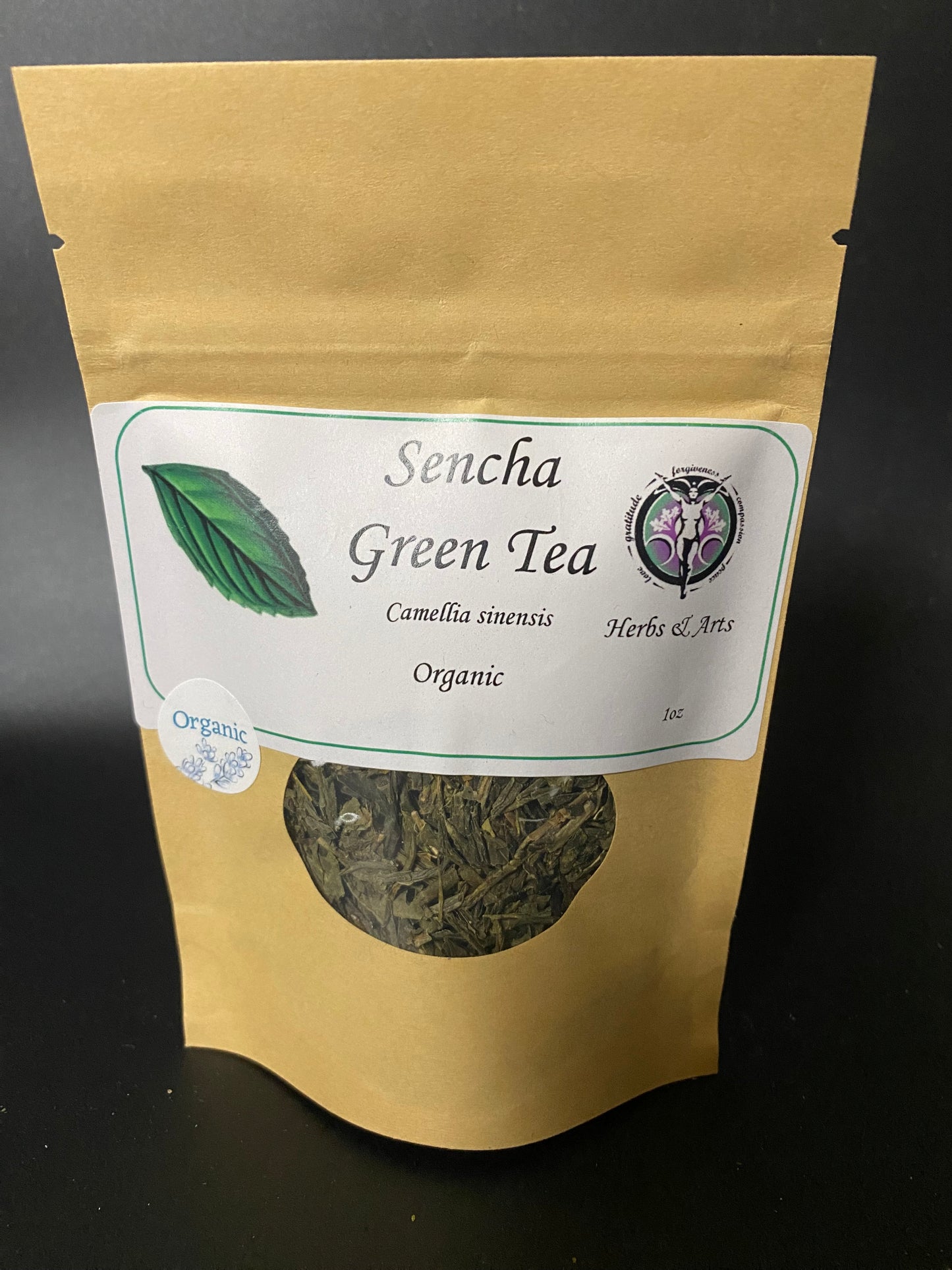 A stand-up kraft paper pouch of Sencha Green Tea with a white label and a circular window showing loose leaf herbal tea inside, photographed against a dark background.
