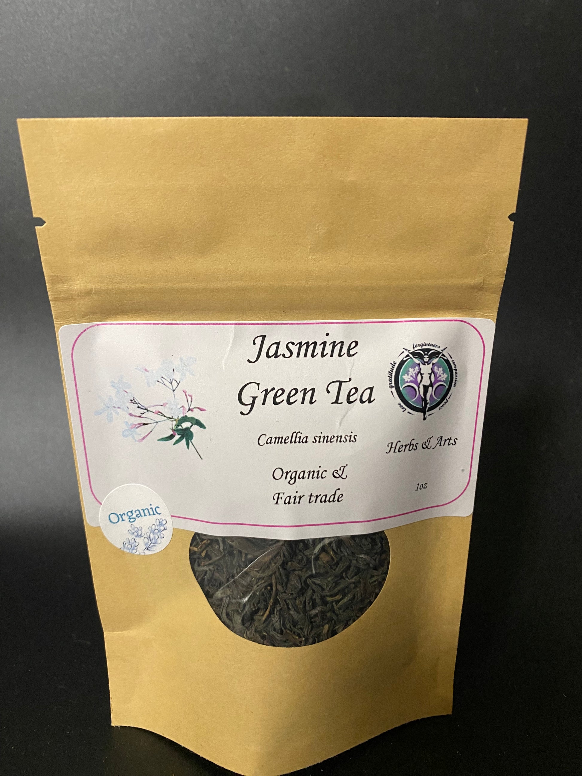 A stand-up kraft paper pouch of Jasmine Green Tea with a white label and a circular window showing the dried herbal tea inside, photographed against a dark background.