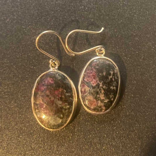 A pair of silver-tone dangle earrings with oval cabochon stones featuring a mottled pattern of pink, green, and dark brown, displayed on a dark textured surface.