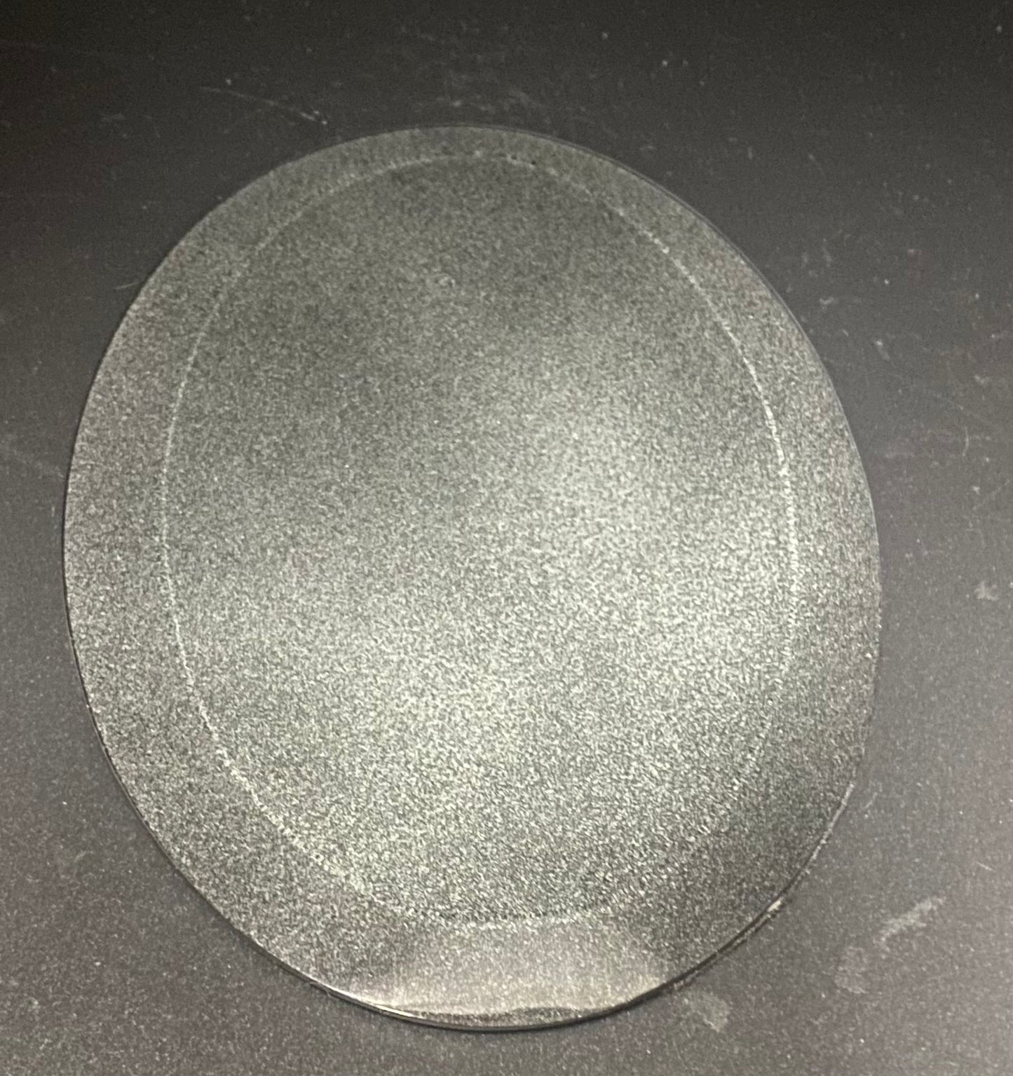 A oval, textured gray glass scrying mirror shown from above on a dark gray surface.